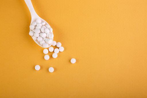 A closeup of a spoon with medical pills on a yellow background