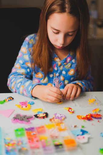 A vertical shot of a Hispanic child making bindeez designs on blurred background