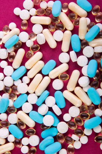 Different medical pills scattered on a pink surface