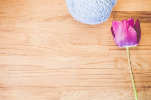 A high angle shot of a purple tulip and a ball of yarn on a wooden surface