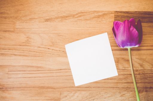 A high angle shot of a purple tulip and a piece of paper on a wooden surface - copy space