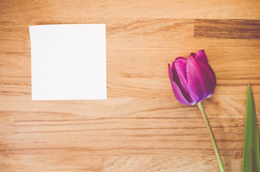 A high angle shot of a purple tulip and a piece of paper on a wooden surface - copy space