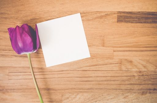 A high angle shot of a purple tulip and a piece of paper on a wooden surface - copy space