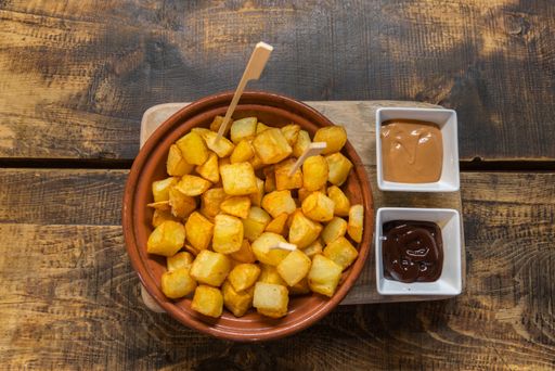 A top view of traditional Spanish food called Patatas bravas with sauces on a wooden table