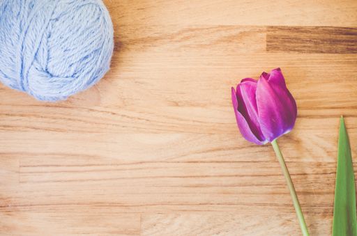 A high angle shot of a purple tulip and a ball of yarn on a wooden surface