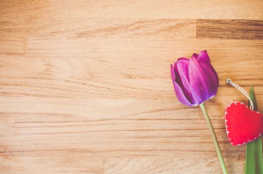 A high angle shot of a purple tulip and a heart-shaped decorative on a wooden surface