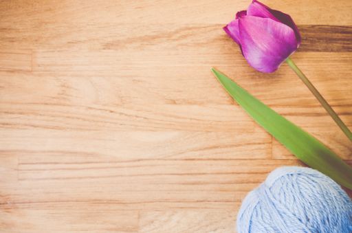 A high angle shot of a purple tulip and a ball of yarn on a wooden surface