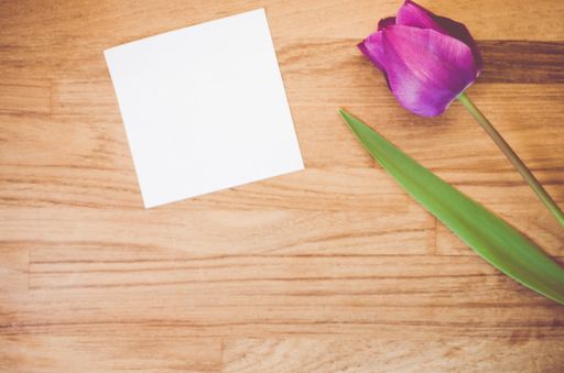 A high angle shot of a purple tulip and a piece of paper on a wooden surface - copy space