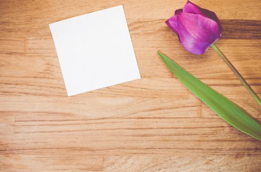 A high angle shot of a purple tulip and a piece of paper on a wooden surface - copy space