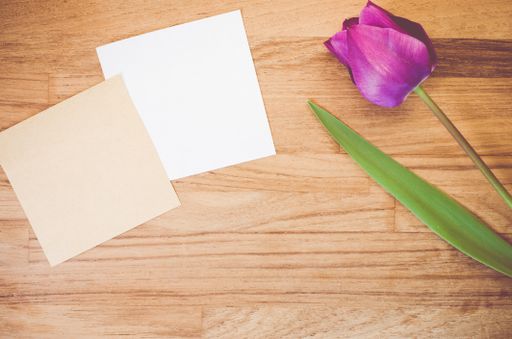A high angle shot of a purple tulip and pieces of paper on a wooden surface
