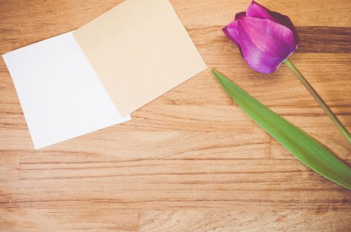 A high angle shot of a purple tulip and pieces of paper on a wooden surface