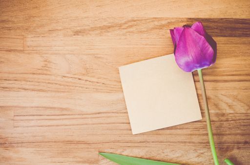 A high angle shot of a purple tulip and a piece of paper on a wooden surface