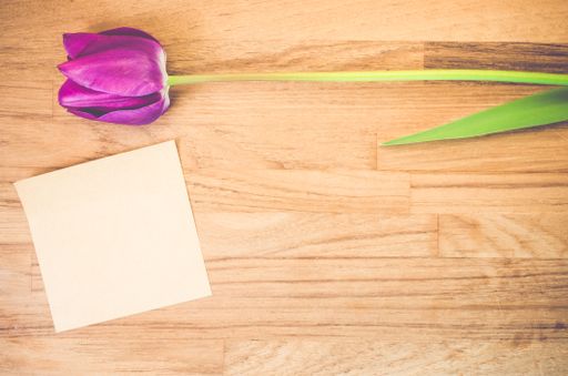 A high angle shot of a purple tulip and a piece of paper on a wooden surface