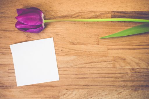 A high angle shot of a purple tulip and a piece of paper on a wooden surface