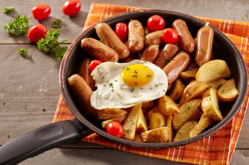 Cocktail sausages and potato wedges are served with fried eggs in a frying pan, ready to eat