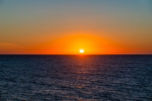 A scenic view of a vibrant red cloudless sunset reflected on the calm sea