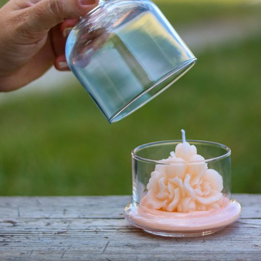 A hand opening a glass jar with a decorative pink candle inside