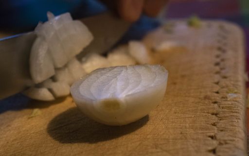 A closeup shot of a man slicing an onion with a knife on a wooden board