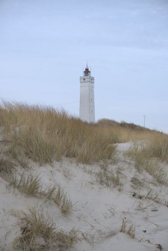 A vertical shot of the lighthouse on a sandy beach on a background of a blue sky