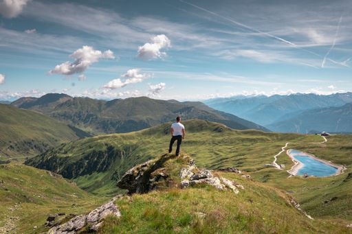 An adult male standing on a hill covered in greenery under the sunlight and a blue cloudy sky