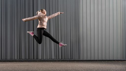 young women in a acrobatic jump in front of a building wall