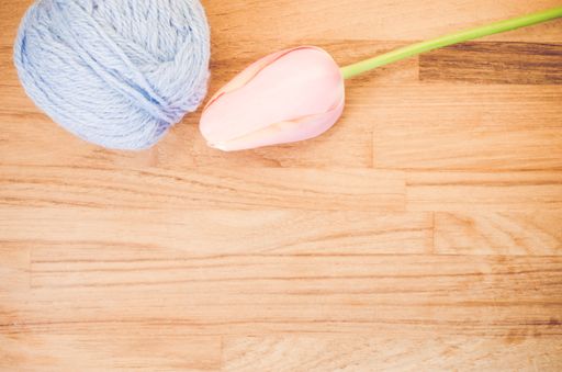 An overhead shot of a pink tulip and a ball of yarn on a wooden surface