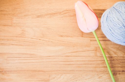 An overhead shot of a pink tulip and a ball of yarn on a wooden surface