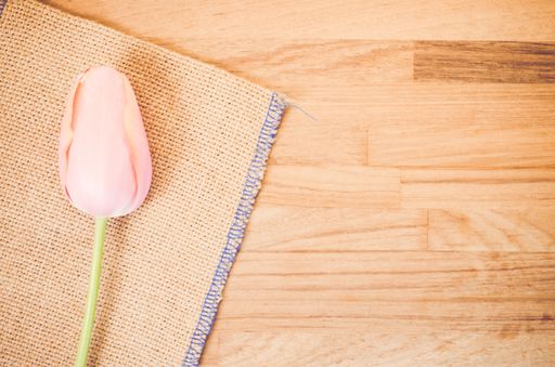An overhead shot of a pink tulip flower against burlap cloth on a wooden table with space for your text