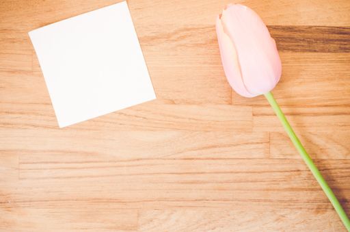 An overhead shot of a pink tulip flower and a blank sticky note on a wooden table with space for your text