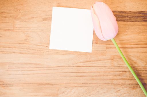 An overhead shot of a pink tulip flower and a blank sticky note on a wooden table with space for your text
