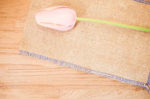 An overhead shot of a pink tulip flower against burlap cloth on wooden table with space for your text