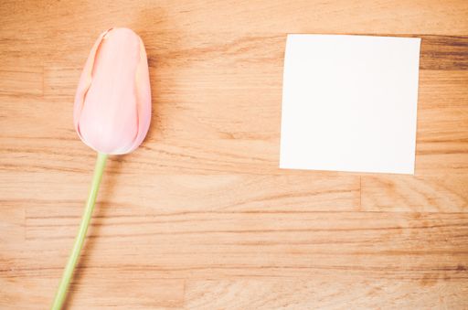 An overhead shot of a pink tulip flower and a blank sticky note on a wooden table with space for your text