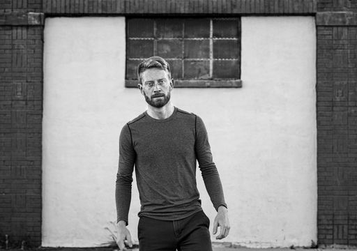 A grayscale shot of an attractive Caucasian male in front of a building and looking at the camera