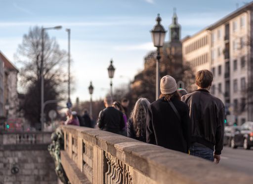 A queue of people standing on a bridge surrounded by buildings under the sunlight in autumn