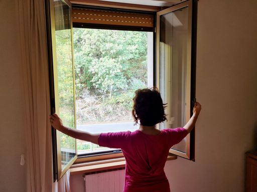 A woman looking from behind opened window to let in the light at home