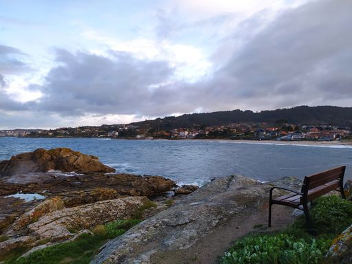 A rocky shore surrounded by the sea and buildings under a cloudy sky on a stormy day