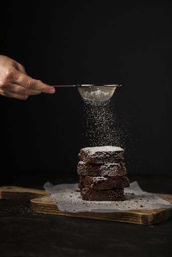 A vertical shot of a hand sprinkling sugar powder in biscuit pile