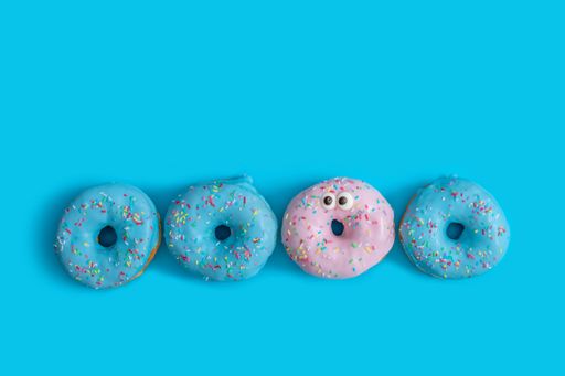 A top view of three blue and one pink donut on a blue background  - the concept of diversity