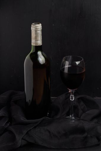 A vertical shot of a bottle of wine and a wineglass by a black background