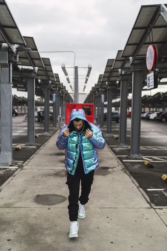 A vertical shot of a stylish man wearing a multicolored down jacket, black trousers, and sneakers
