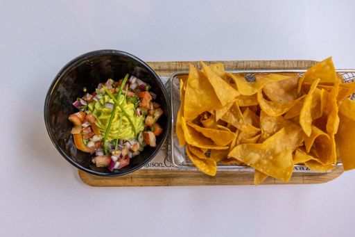 A top view of chips, salad and a glass of red wine on a white table