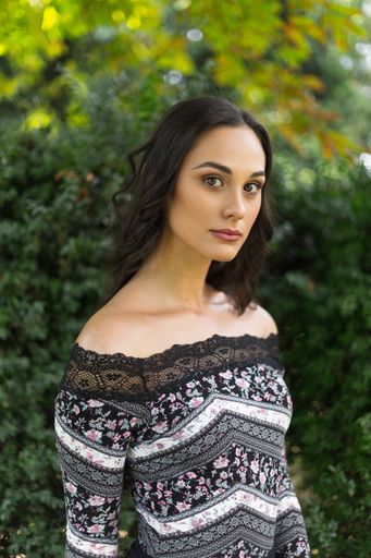 A vertical shot of a young Caucasian woman with long brunette hair posing in the park