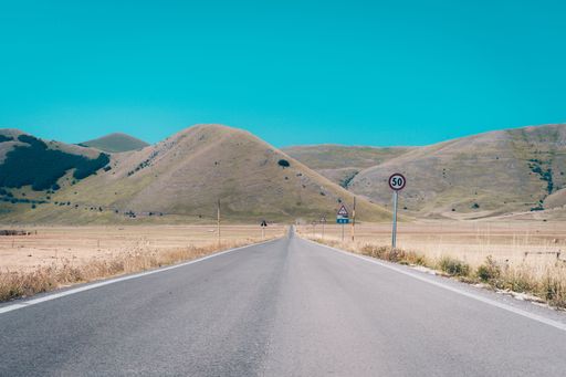 A scenic view of an asphalt road in a field with "50"speed limit sign against mountains on a sunny day
