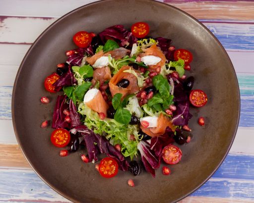 A top view shot of the fresh salmon with tomatoes, pomegranate, lettuce salad on a plate