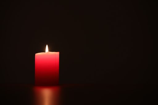 A closeup shot of a brightly glowing candle with a light reflection on a table surface
