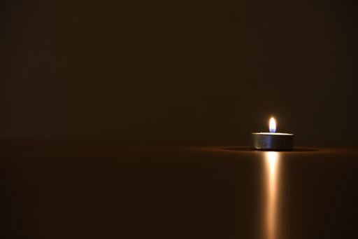 A closeup shot of a burning small candle with a light reflection on a table surface