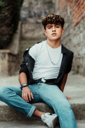 A vertical shot of a young Caucasian man with curly hair and casual style sitting on the stairs