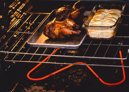 A closeup of chicken grill and rolls in an electric oven