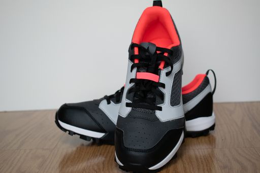 A closeup shot of a pair of training shoes against a wall on a wooden floor