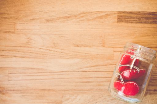 A top view closeup of a plastic white transparent jar with three sewn hearts on a wooden table